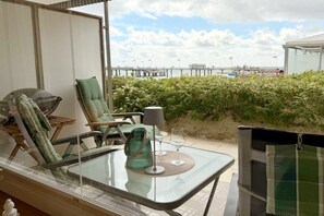 Ein Balkon mit einem Glastisch, zwei Stühlen, einem grünen Kissen, einer Glaskaraffe und zwei Weingläsern.