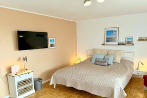 Ein Schlafzimmer mit Bett, Fernseher, Nachttisch, Lampe und Wandregal mit Bildern.