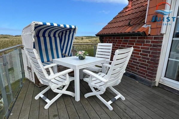 A deck with white furniture, including a table and chairs, and a striped beach umbrella. - Apartment 260 - Dünenliebe (Juist)