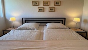 Una cama doble con cabecera de madera, dos mesitas de noche con lámparas y cuadros enmarcados en la pared.