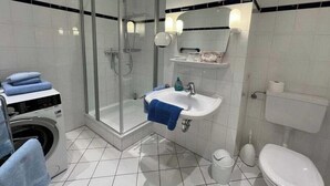 Un baño con ducha de vidrio, lavabo con toalla, inodoro y lavadora.
