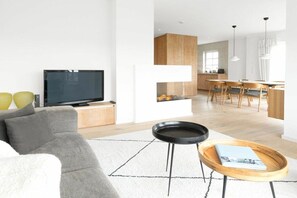 A modern living room with a flat-screen TV, a grey sofa, and a coffee table with a magazine. - 238 - Holiday home Watt (Juist)