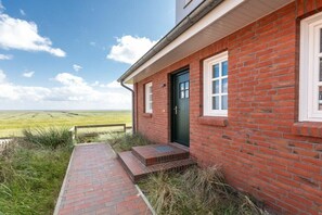 A red brick building with a green door, a small porch, and a view of the countryside. - 238 - Holiday home Watt (Juist)