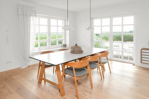 A dining area with a table and chairs, large windows, and a view of greenery. - 238 - Holiday home Watt (Juist)
