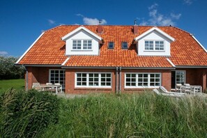 A two-story house with a red-tiled roof, white-framed windows, and a brick exterior. - 238 - Holiday home Watt (Juist)