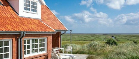 A house with a red-tiled roof, a brick exterior, and a view of a flat landscape.