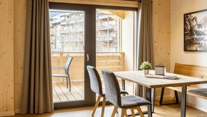 Una habitación con decoración de madera, una puerta de vidrio corredera que da a un balcón exterior, una mesa con sillas y un cuadro en la pared.
