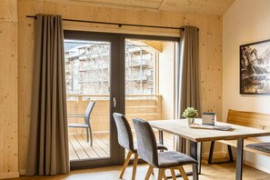 Une pièce au décor intérieur en bois, une porte-fenêtre coulissante donnant sur un balcon extérieur, une table avec des chaises et un tableau encadré au mur.