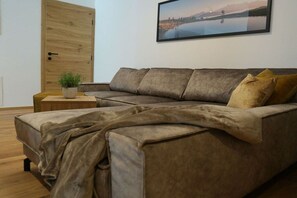 A modern living room with a sectional sofa, a small side table with a plant, and a framed picture on the wall. - Apartment in Rauris with swimming pool (Rauris)