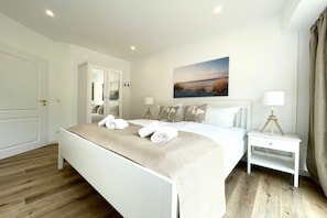 A hotel room with a bed, a bedside table with a lamp, a wardrobe, and a painting on the wall. - Holiday apartment with 1 bedroom (Cuxhaven)
