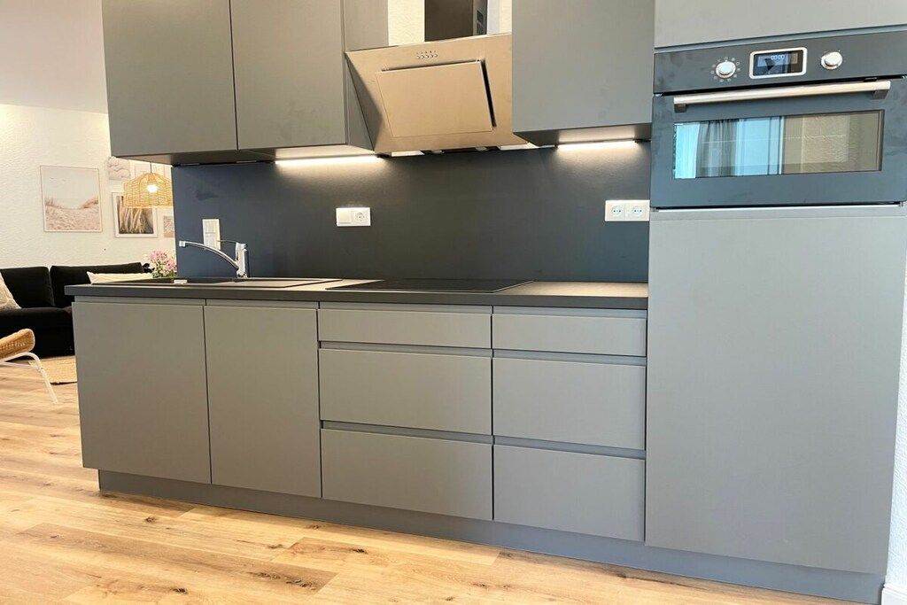 A modern kitchen with grey cabinetry, a built-in oven, and a stainless steel range hood.
