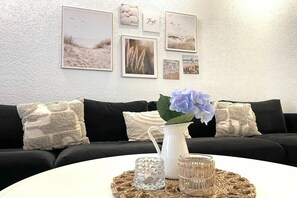 A living room with a black sofa, a white coffee table, and a wall decorated with framed pictures. - Holiday apartment with 1 bedroom (Cuxhaven)