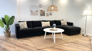En moderne stue med en sort sofa, et hvidt sofabord og en stor plantepotte.