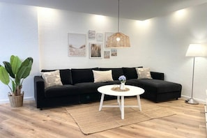 A modern living room with a black sofa, a white coffee table, and a large potted plant. - Holiday apartment with 1 bedroom (Cuxhaven)