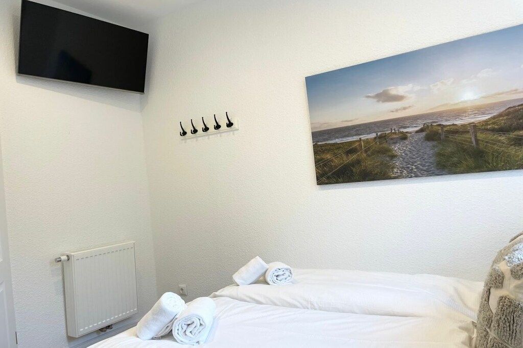 Ein Hotelzimmer mit einem Bett, einem Wandfernseher, einem Strandbild und einer Heizung.