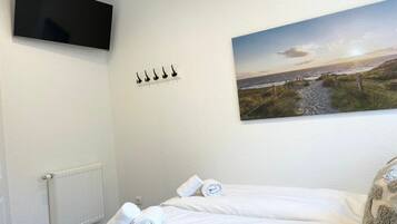 Ein Hotelzimmer mit einem Bett, einem Wandfernseher, einem Strandbild und einer Heizung.