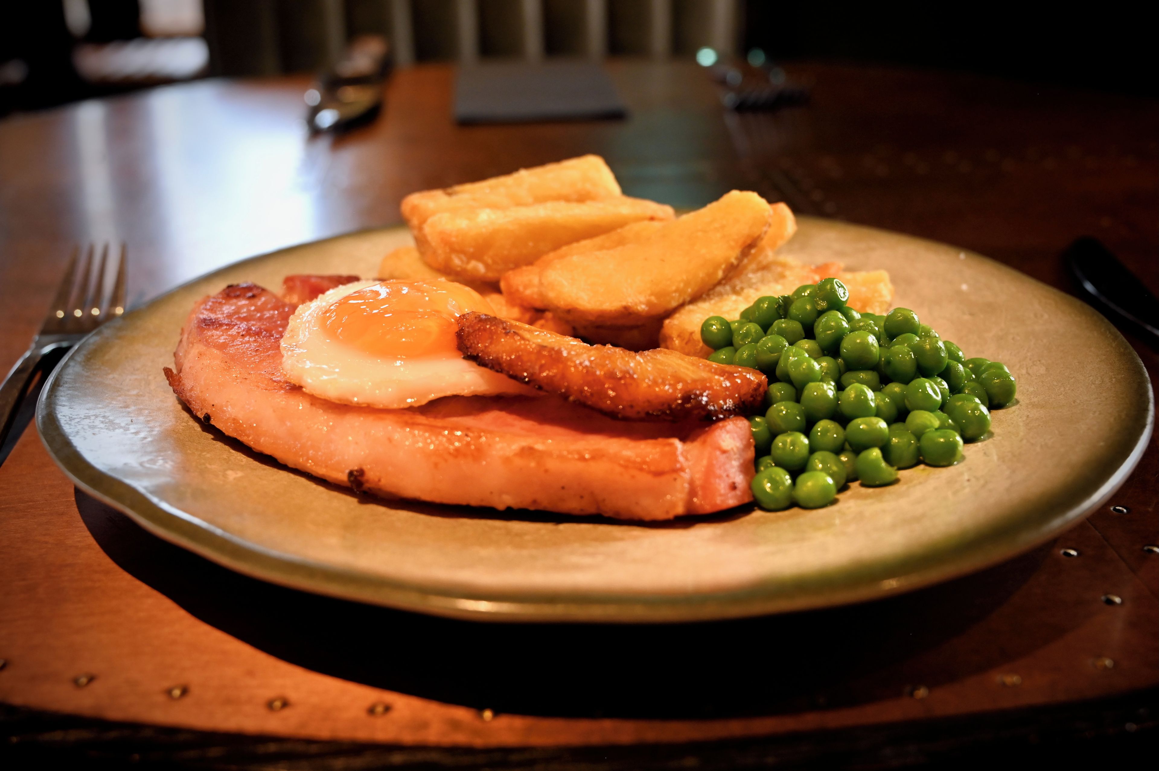 A plate with a slice of ham, a fried egg, toast, and peas.