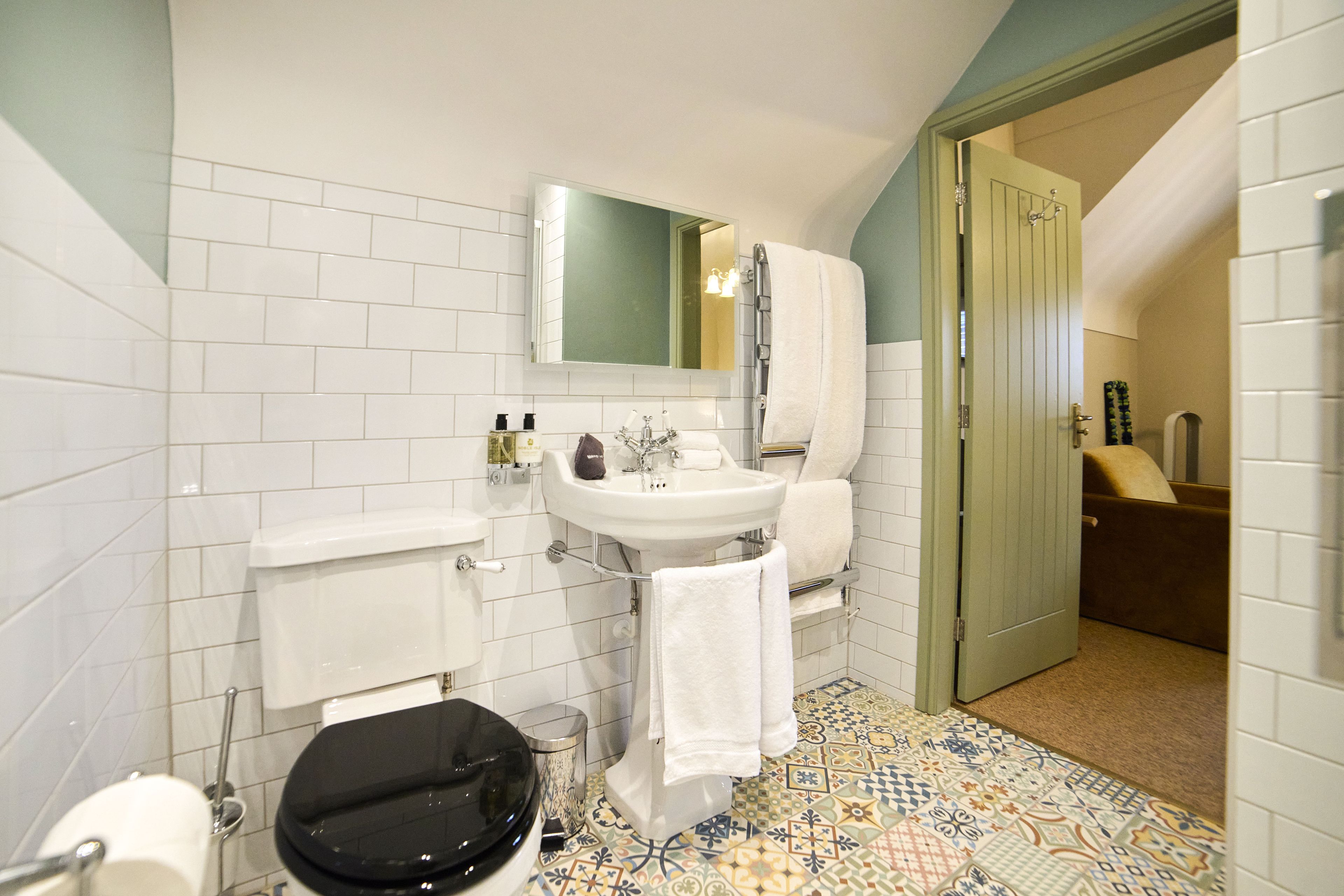 Un baño con inodoro blanco, lavamanos, espejo y zona de ducha.