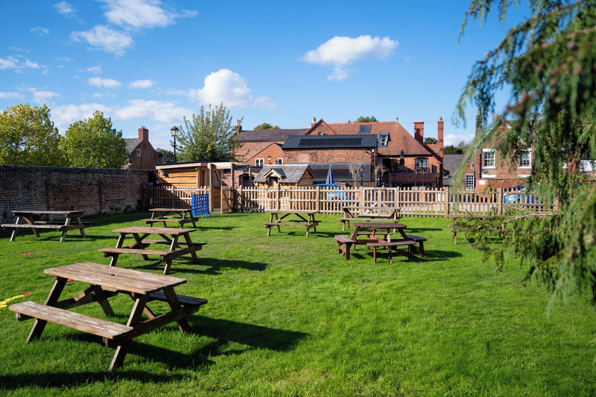 A grassy outdoor area with picnic tables and a brick building in the background.