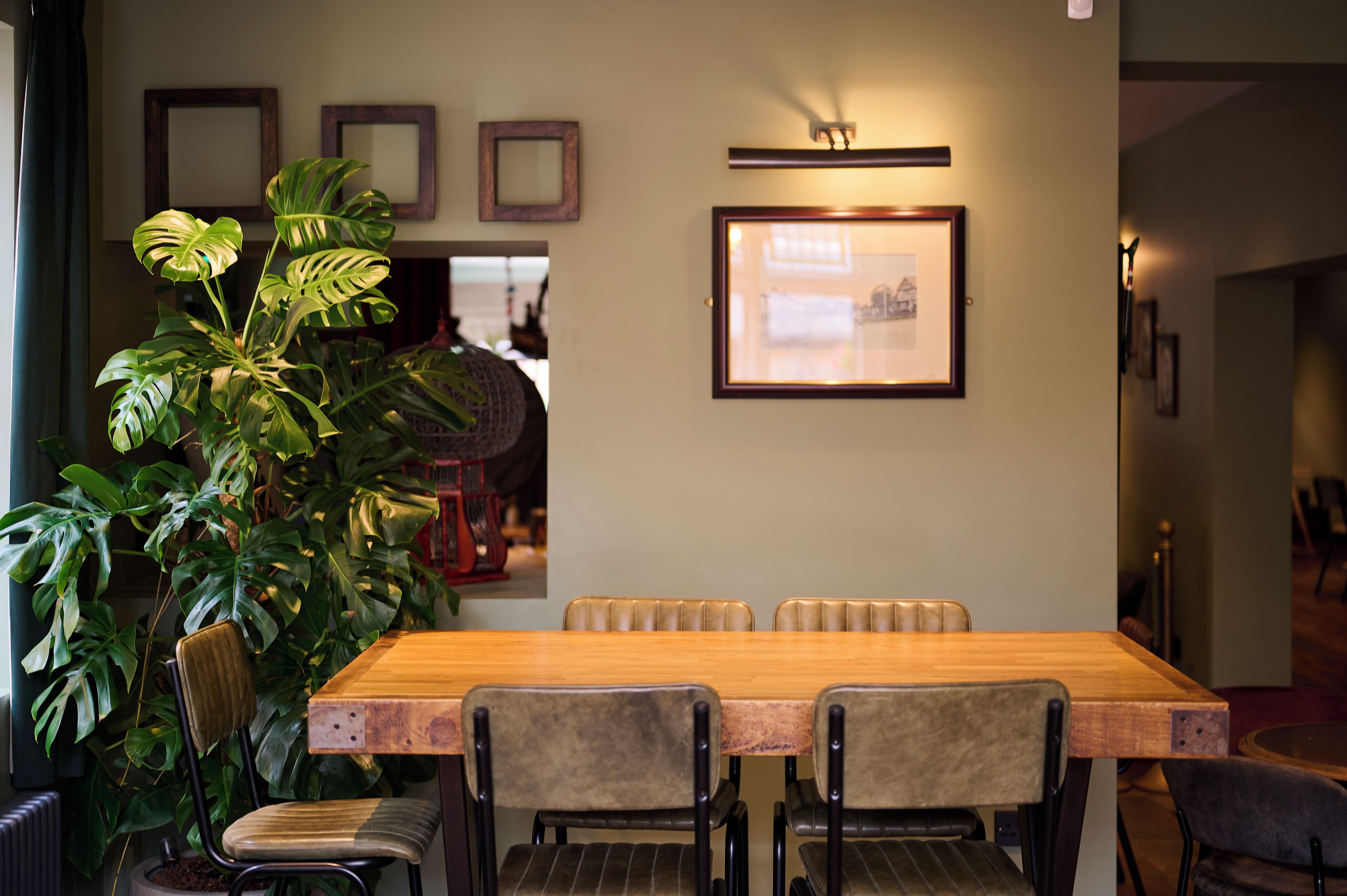 A dining area with a wooden table, four chairs, and a large potted plant.