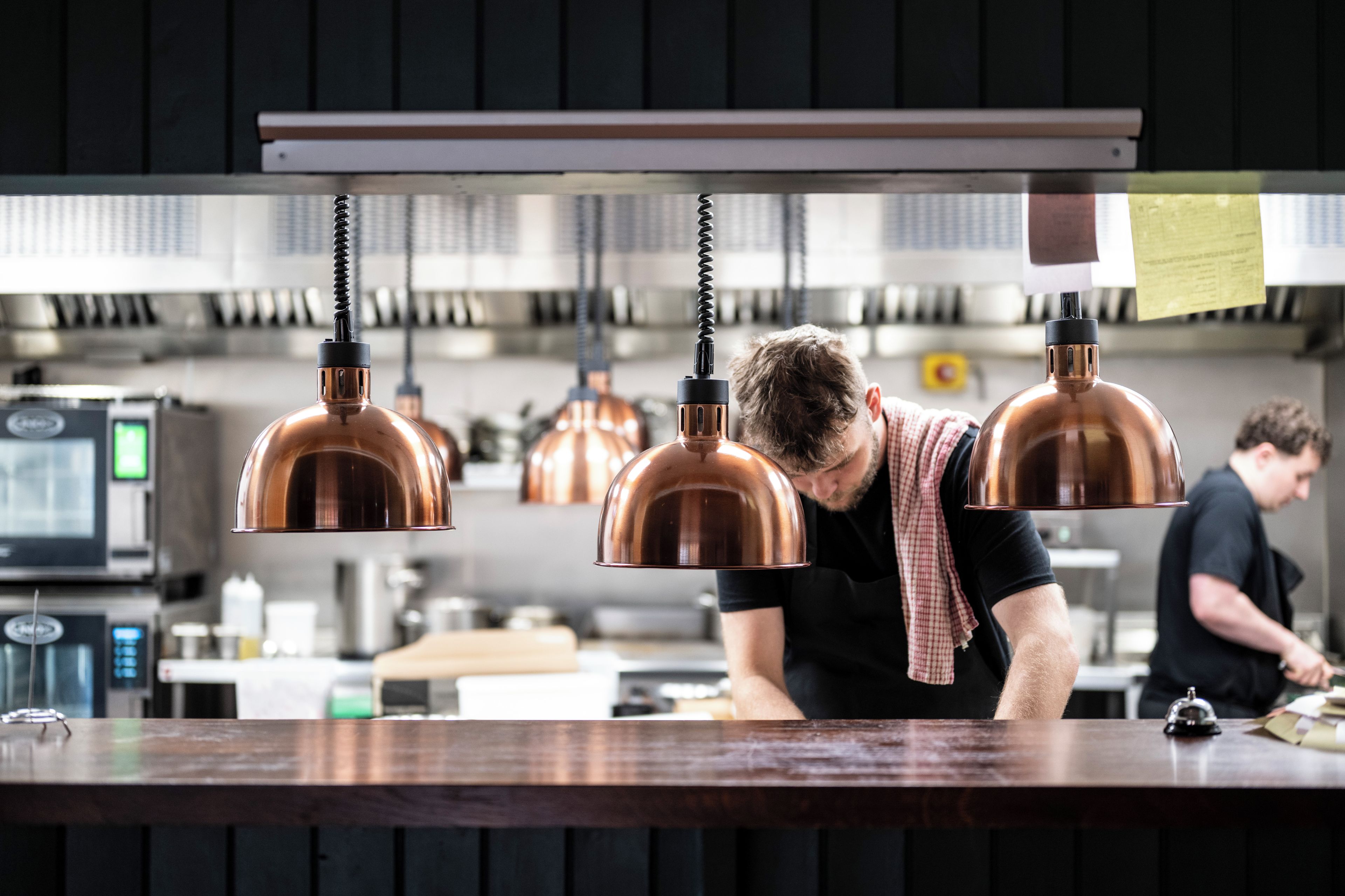 A kitchen with copper pendant lights, a wooden countertop, and a person working at the counter.