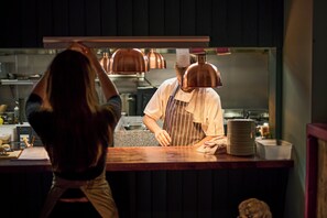 A person standing at a counter with a reflective surface behind them, possibly in a kitchen or service area. - The Bear  (Tattenhall)