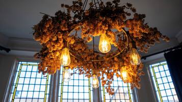 Un candelabro con múltiples bombillas, rodeado de flores secas, en una habitación con ventanas amplias.