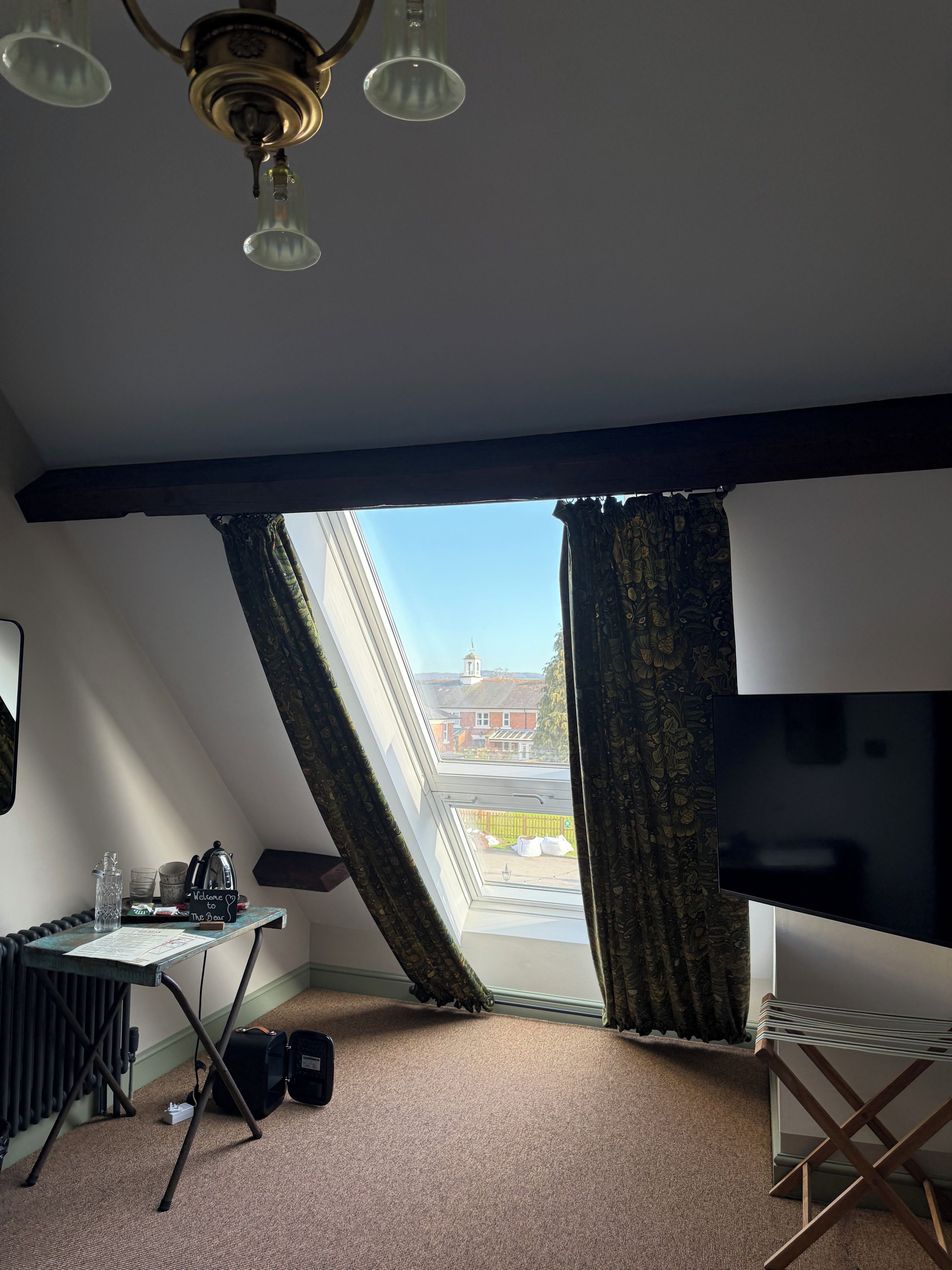 Una habitación con techo inclinado, un televisor, un escritorio con hervidor, una taza y un cartel que dice 'Welcome to The Bear'.