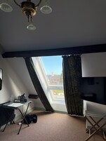 A room with a sloped ceiling, a television, a desk with a kettle, a cup, and a sign that reads 'Welcome to The Bear.'