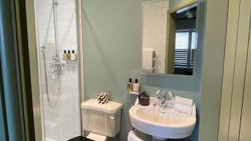 Un baño con ducha envuelta en vidrio, un lavamanos blanco y un inodoro.