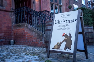 Un letrero que dice 'The Bear Tattenhall Christmas' con una ilustración de un oso e invitación a reservar.