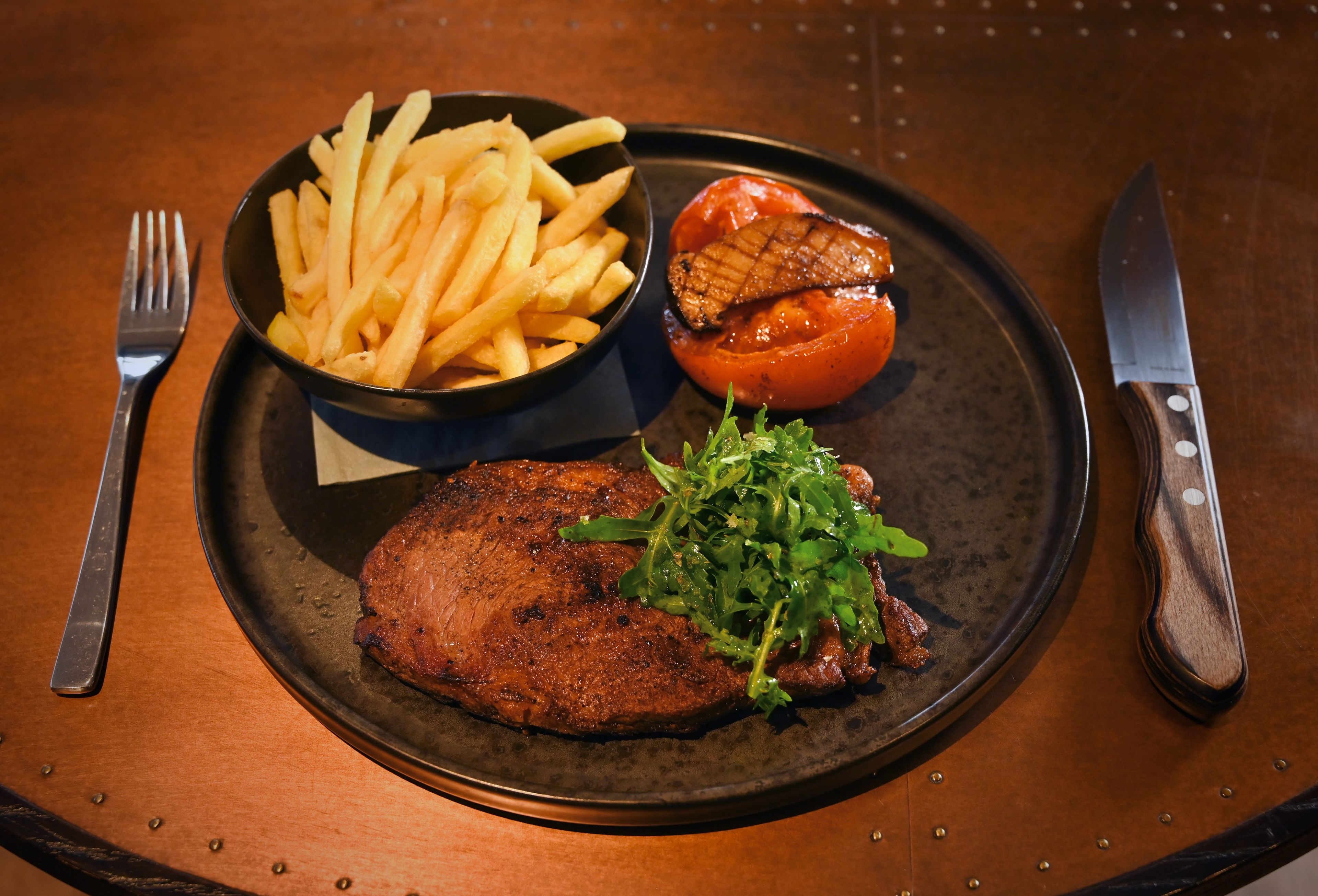 Un plato con un bistec, papas fritas, un tomate a la parrilla y una ensalada.