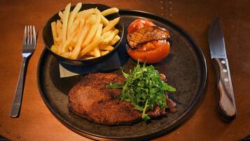 Un plato con un bistec, papas fritas, un tomate a la parrilla y una ensalada.