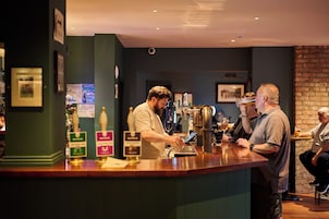 A bar area with a counter, beer taps, and a person serving a drink.