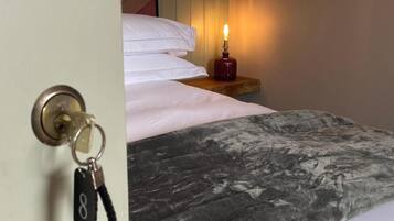 Habitación de hotel con cama, mesita de noche con vela encendida y puerta con llave.