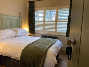 A hotel room with a bed, a radiator, a window with blinds, and a door with a key. - The Bear  (Tattenhall)