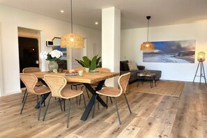 Un coin repas avec une table en bois et des chaises en osier, un salon avec un canapé et un tableau, ainsi qu’une lampe sur pied.