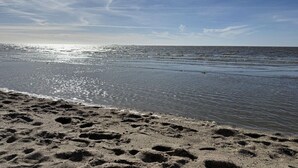 En strand med fodspor i sandet og et roligt hav under en klar himmel.