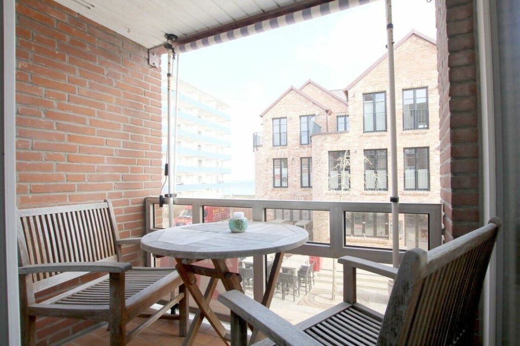 Un balcón con una mesa redonda y dos sillas de madera, con vista a un edificio de ladrillo y múltiples ventanas.