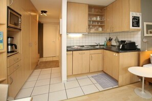 Cozinha compacta com armários de madeira, micro-ondas, cafeteira e torradeira.