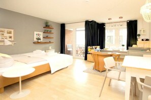 Une chambre à coucher moderne avec un lit, des tables de chevet, un bureau et une chaise. On y trouve une fenêtre avec des rideaux, une porte donnant sur un espace extérieur et un lustre.