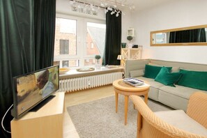 A living room with a sofa, a television, a small round table, and a window with curtains. - Holiday apartment with 1 bedroom (Wyk auf Föhr)