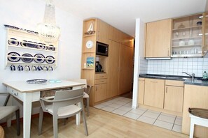 A compact kitchen with wooden cabinets, a microwave, and a tiled backsplash. - Holiday apartment with 1 bedroom (Wyk auf Föhr)