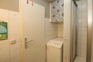 A bathroom with a white door, a washing machine, and a shower area. - Holiday apartment with 1 bedroom (Wyk auf Föhr)