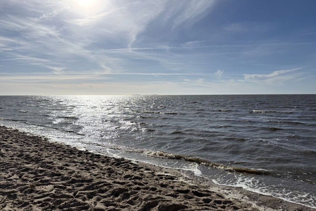 Ein Strand mit Sand und Wellen, ein klarer Himmel und die strahlende Sonne.