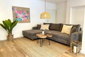 Ein Wohnzimmer mit grauem Sofa, einem gewebten Couchtisch, einer Topfpflanze und einem Bild an der Wand.