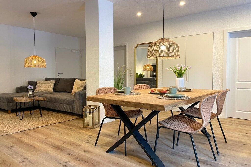 A modern living room with a sofa, coffee table, and dining table with chairs. There is a hanging light fixture above the dining table.