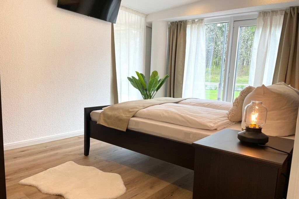 A bedroom with a bed, bedside table, lamp, and a plant.