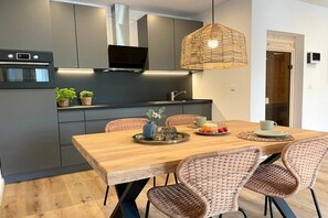 A modern kitchen with a wooden dining table, wicker chairs, and a hanging light fixture. - Holiday apartment with 1 bedroom (Cuxhaven)