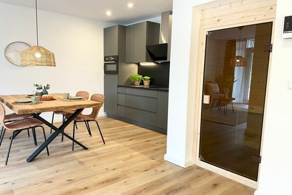 A modern kitchen with grey cabinets, a wooden dining table, and a glass sliding door leading to a living area. - Holiday apartment with 1 bedroom (Cuxhaven)